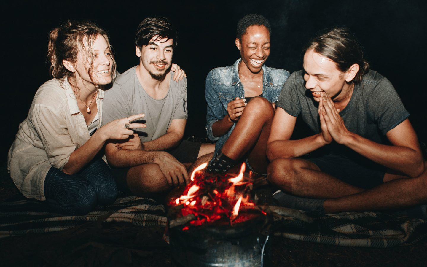 Young adults laughing in front of a fire in the dark night.