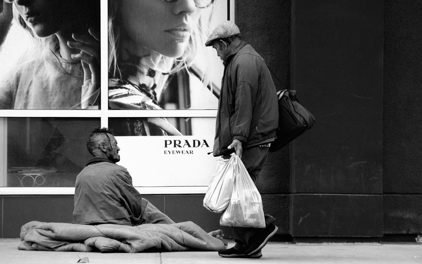 Two men on a street near a Prada storefront window.