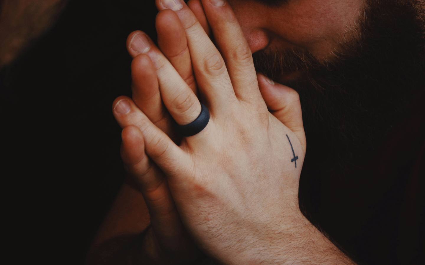 A man with a cross tattoo on his hand folds his hand in prayer.