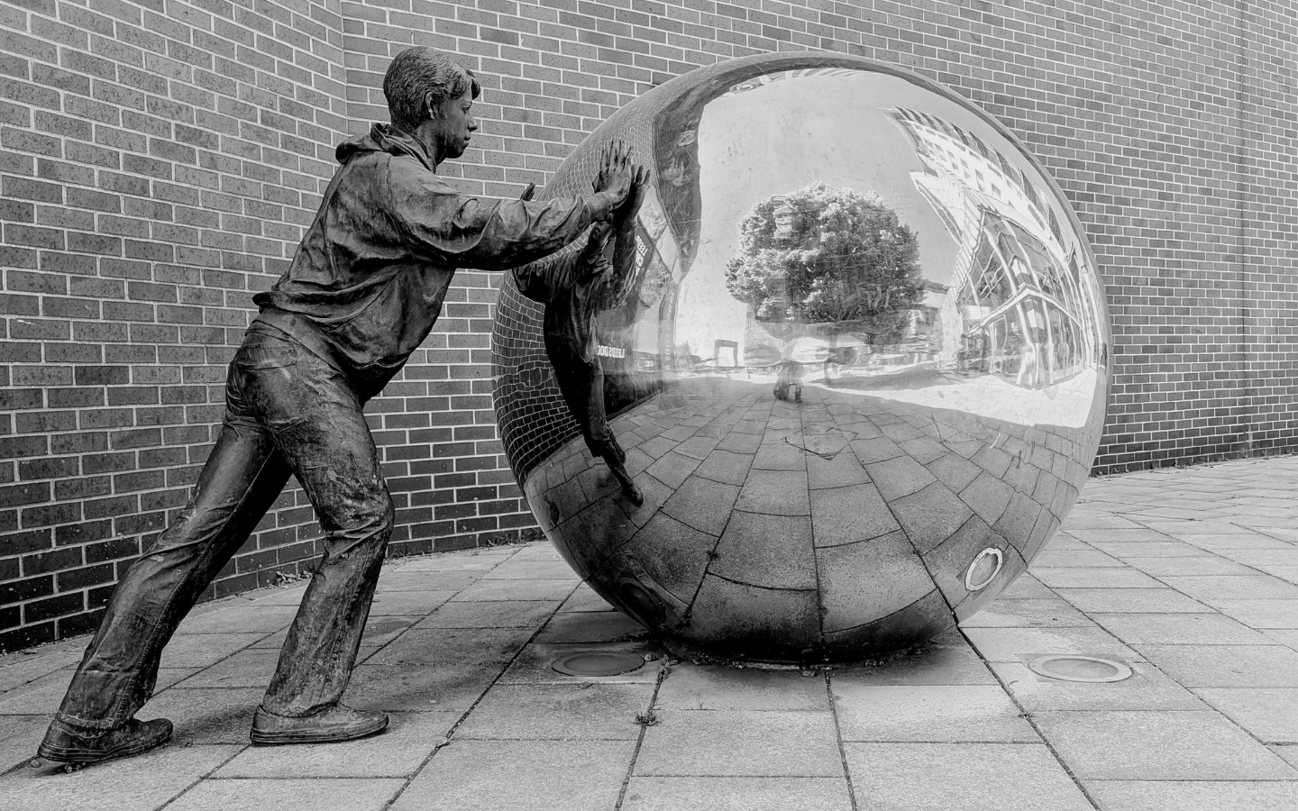 A monochrome sculpture of a man pushing a reflective sphere.