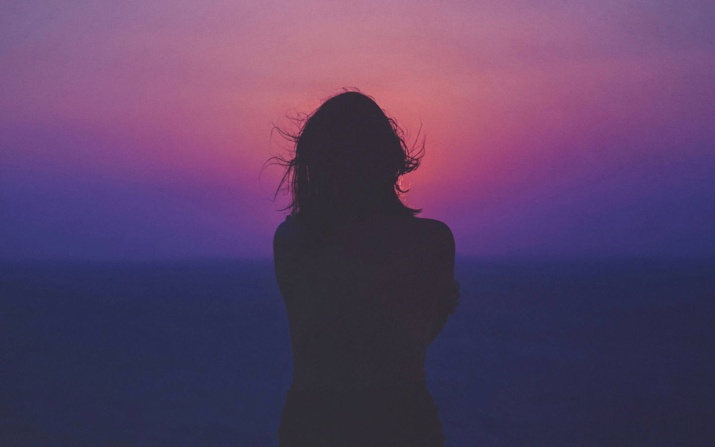 A silhouette of a woman facing a purple sunset.