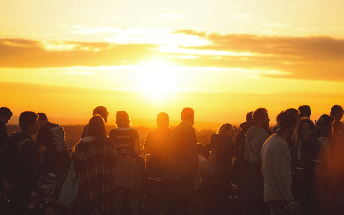 A crowd of people watches a sunrise (or sunset).