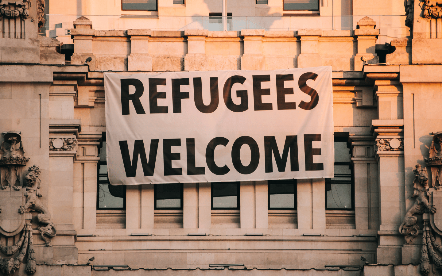 A sign reading “Refugees Welcome” hanging on a building.