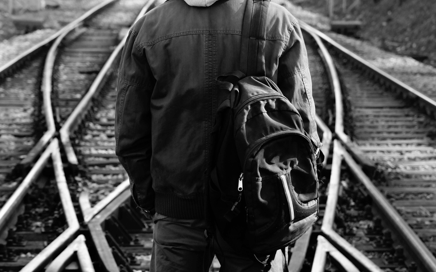 A man stands on a set of diverging train tracks deciding which one to take.