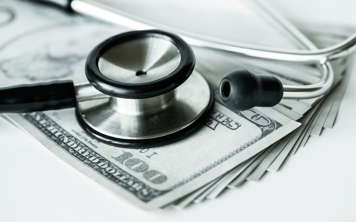 A stethoscope on top of a stack of $100 bills.