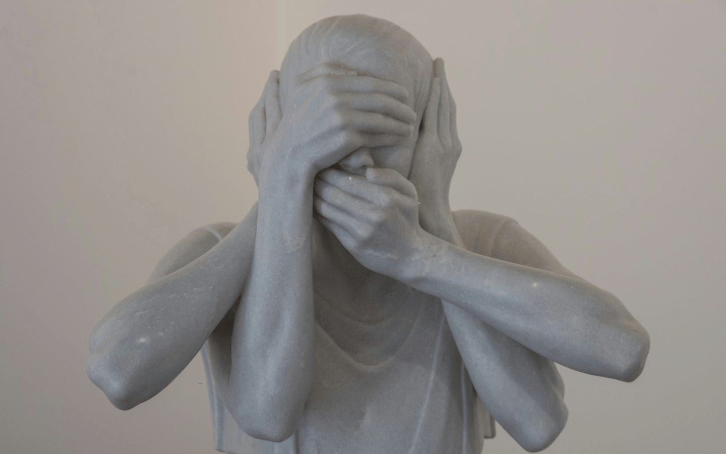 A marble statue of a head with hands covering its eyes, ears, and mouth.