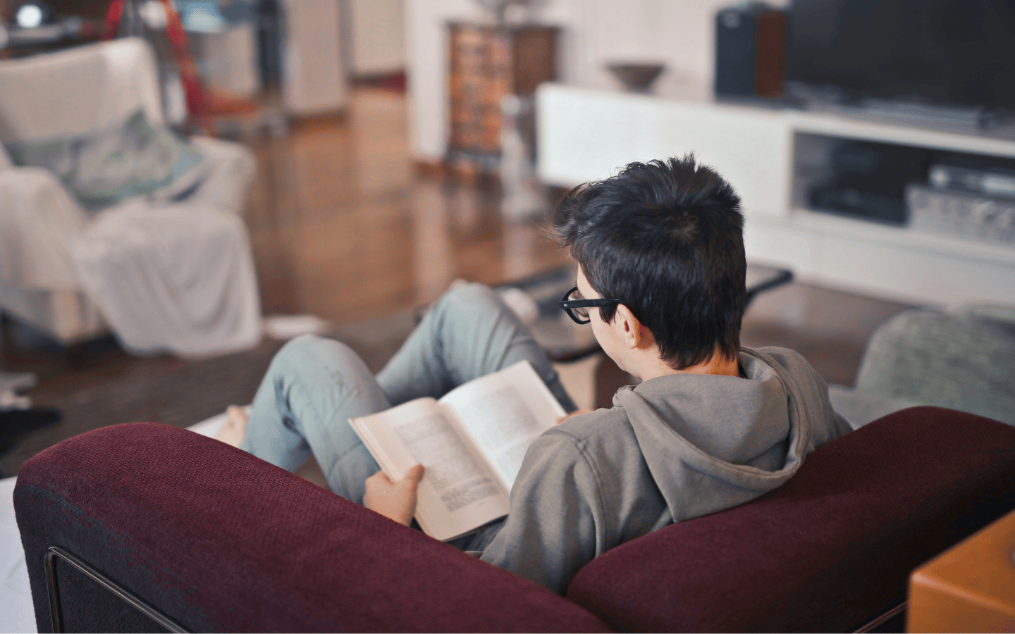 A teenage boy reads a book in a comfortable chair.