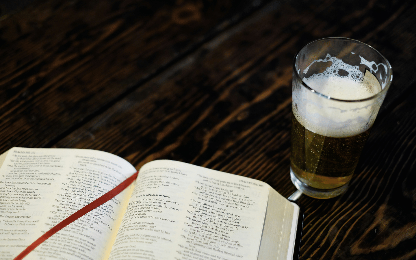 A beer sits next to an open Bible.