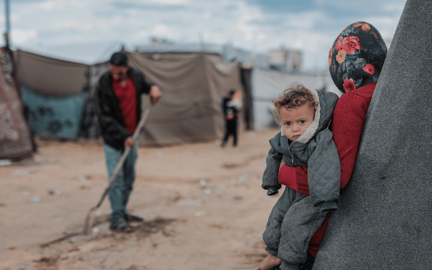 A woman holds a young child as others clean up a refugee camp in Gaza.