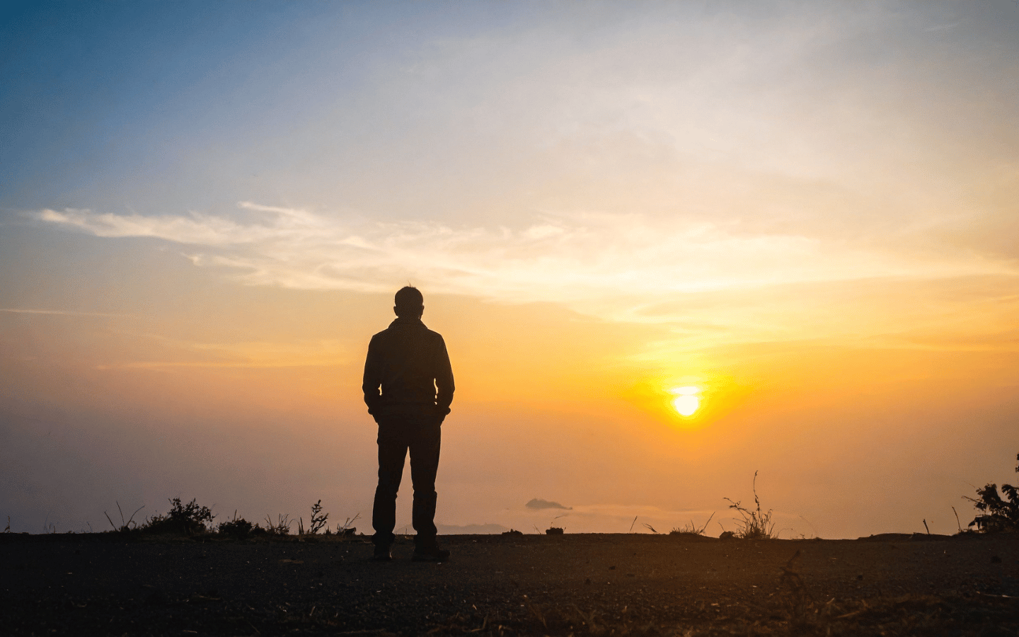 A silhouette of a man standing in reflection, with the sun on the horizon.