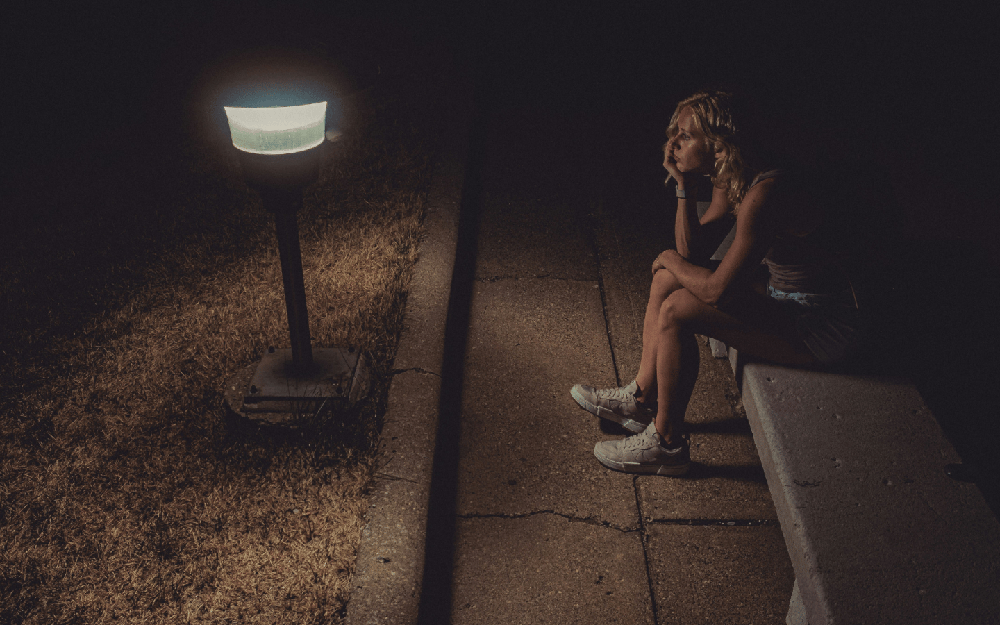 A woman sits in the dark near a lamp, contemplating.