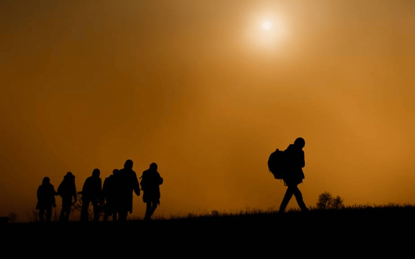 The silhouette of a group of immigrants walking under a hot sun.