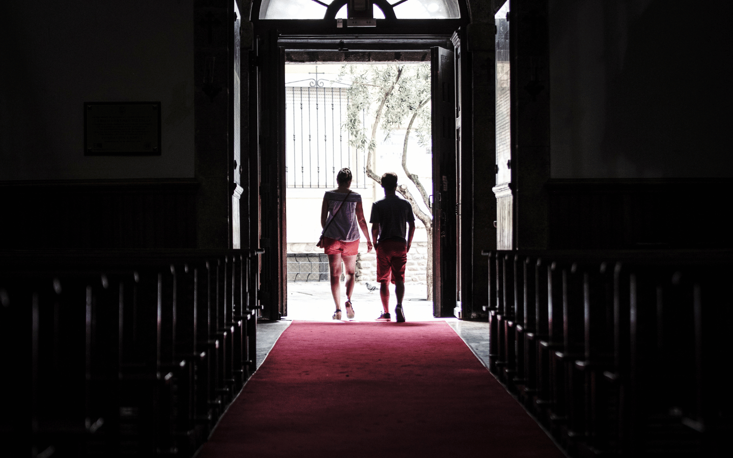 An image of two people walking out of a dark church sanctuary and into sunlight.