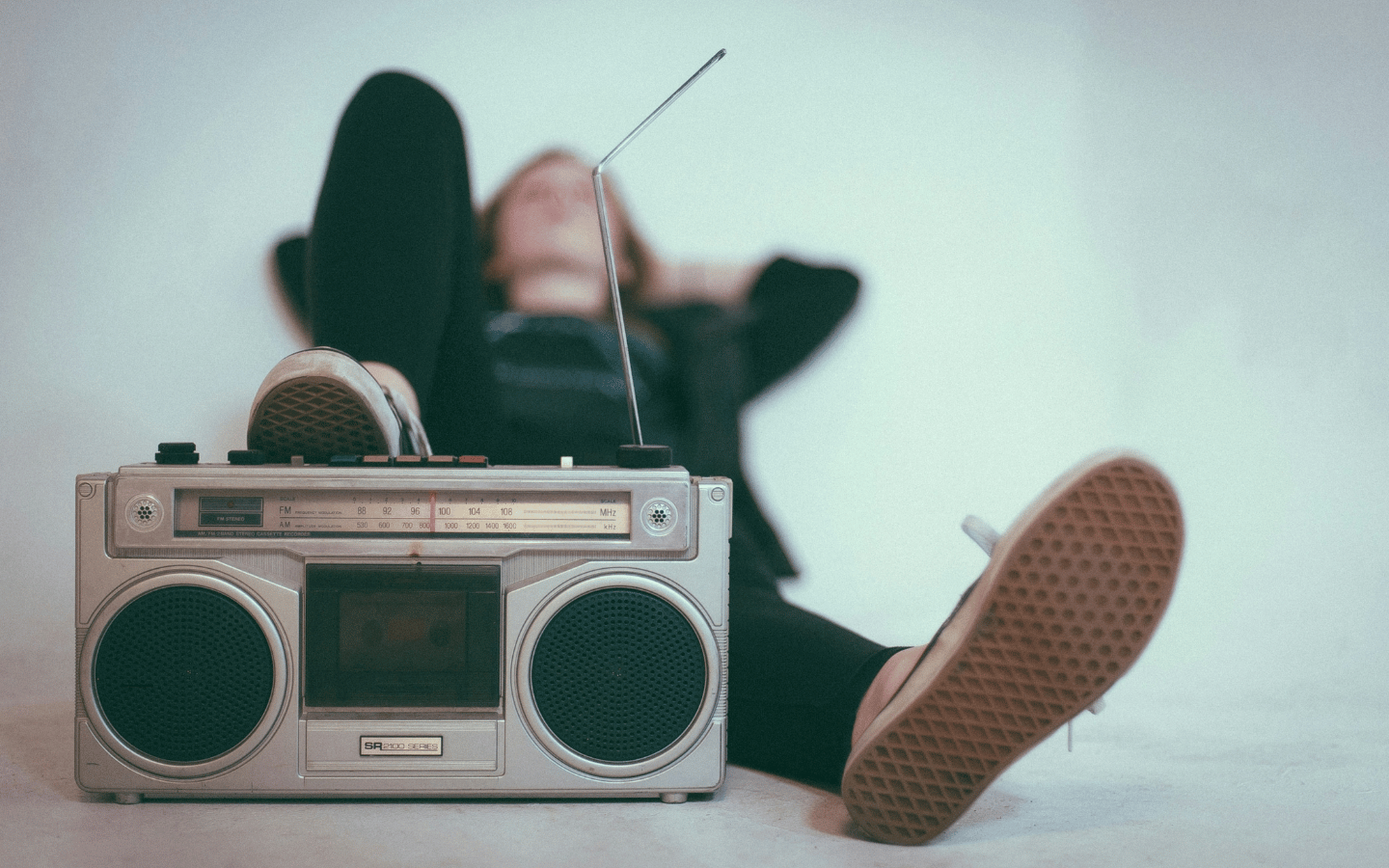 A person leans back and listens to music from a boom box.